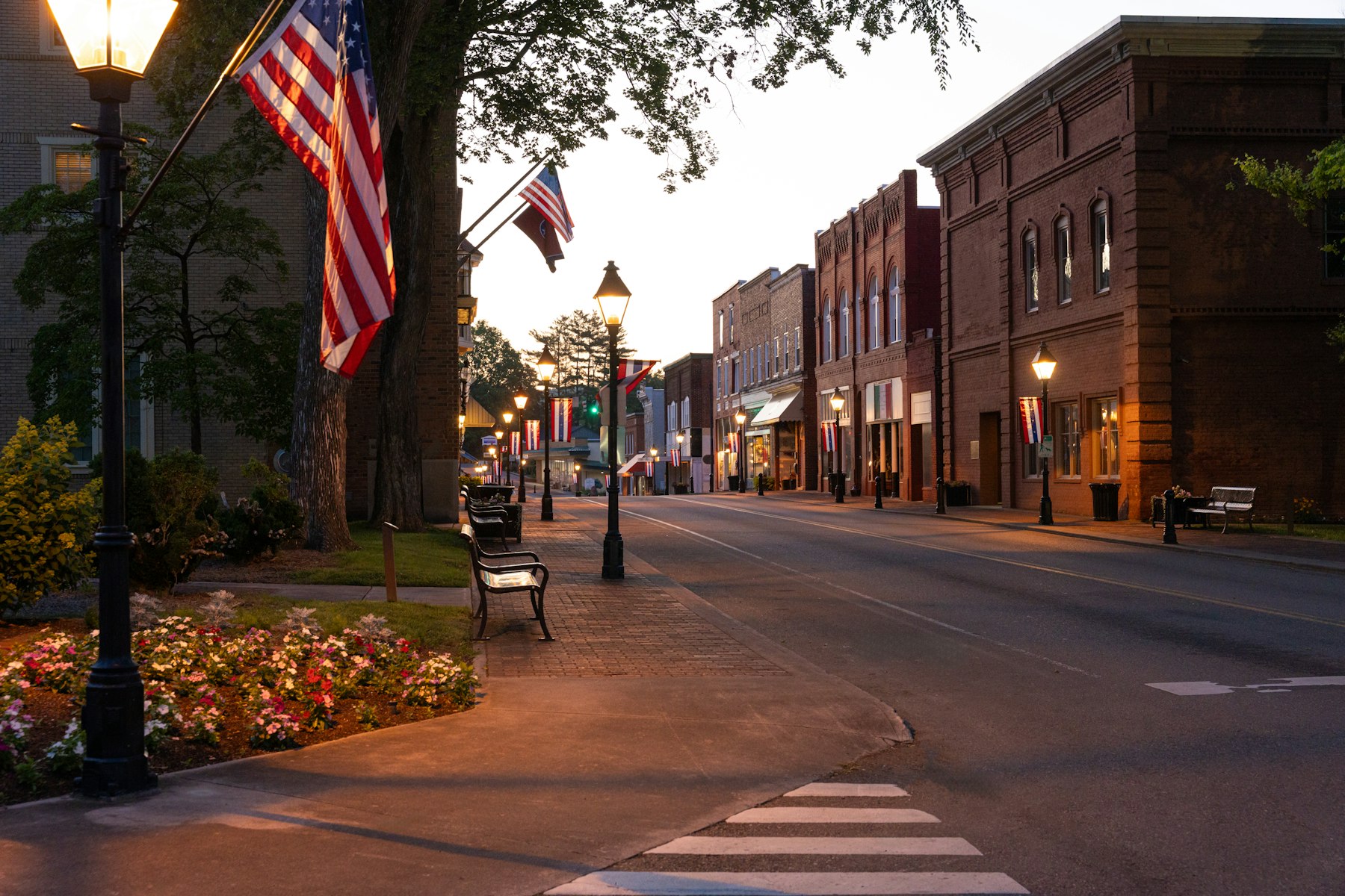 A small town main street at dusk, lit by street lamps